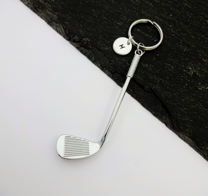 Puede incluir: Llavero de club de golf plateado con un dije inicial plateado. El dije tiene la letra "H" grabada.