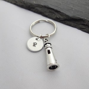Puede incluir: Llavero de plata con un dije de faro y un dije redondo con la letra R grabada.