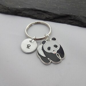 May include: A silver keychain with a black and white panda charm and a silver charm with the letter "R" engraved on it.