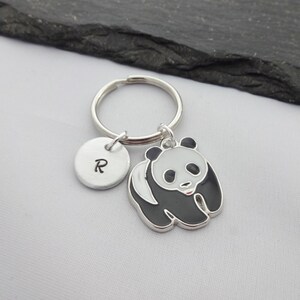 May include: A silver keychain with a black and white panda charm and a silver charm with the letter "R" engraved on it.