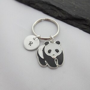 May include: A silver keychain with a black and white panda charm and a silver charm with the letter "R" engraved on it.