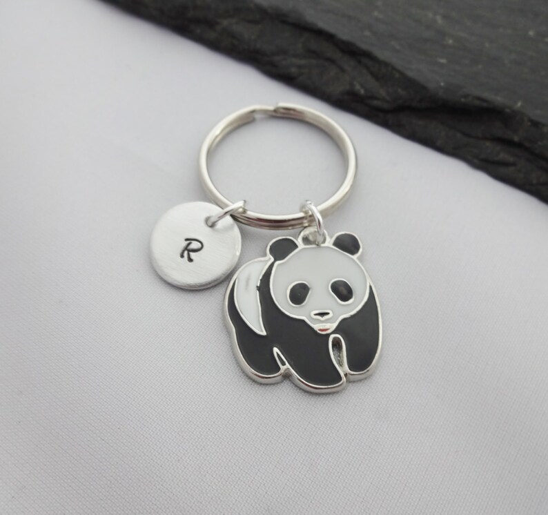 May include: A silver keychain with a black and white panda charm and a silver charm with the letter "R" engraved on it.