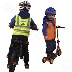 May include: Two children wearing safety vests with the text "Safety First ABC School" on them. One child is riding a bicycle and the other is riding a scooter.