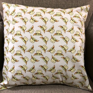 May include: A white pillow with a repeating pattern of a green, cartoon character with large eyes and pointy ears. The character is holding a white banner.