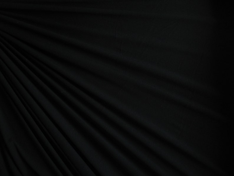 May include: Black fabric with a smooth, wrinkle-free texture. The fabric is draped and folded, creating soft, flowing lines.