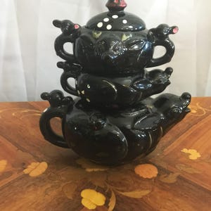 May include: A set of three black ceramic teapots with white polka dots and mouse-shaped handles. The teapots are stacked on top of each other.