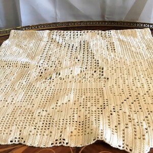 May include: A white crocheted tablecloth with a delicate pattern. The tablecloth is made of fine yarn and has a scalloped edge.
