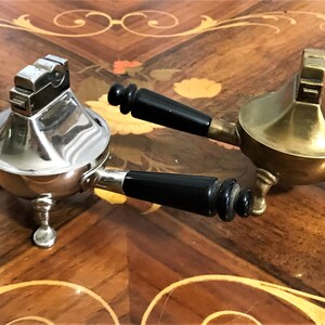 May include: Two vintage table lighters with black handles. One is silver and the other is gold.