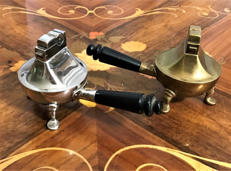 May include: Two vintage table lighters with black handles. One is silver and the other is gold.