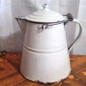 May include: White enamel pitcher with a wooden handle and a lid. The pitcher has a speckled finish and a worn look.