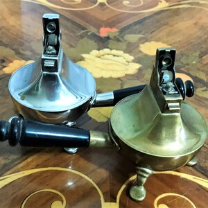 May include: Two vintage table lighters with black handles. One is silver and the other is brass.