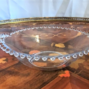K&ouml;nnte beinhalten: Eine klare Glassch&uuml;ssel mit einem perlenbesetzten Rand und Griffen. Die Sch&uuml;ssel steht auf einem Holztisch.