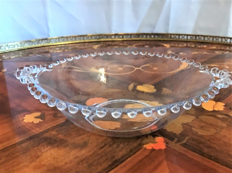 K&ouml;nnte beinhalten: Eine klare Glassch&uuml;ssel mit einem perlenbesetzten Rand und Griffen. Die Sch&uuml;ssel steht auf einem Holztisch.