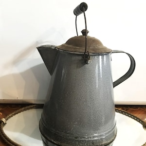 May include: Vintage gray enamelware coffee pot with a speckled finish, a brown lid, and a black handle. The pot has a spout and a wire handle with a wooden grip. A classic kitchenware item.