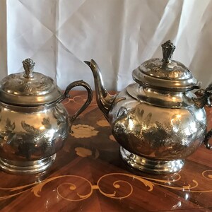 May include: A silver tea set with an ornate design. The set includes a teapot and a sugar bowl.