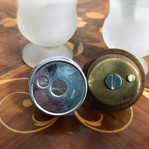 May include: Two vintage lighters, one silver with a black flint and the words "JAPAN" on the bottom, and one brass with a black flint and a gold screw.