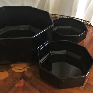 Pode incluir: Tr&ecirc;s tigelas de vidro octogonais pretas de tamanhos diferentes, aninhadas umas nas outras. As tigelas s&atilde;o feitas de vidro preto brilhante e t&ecirc;m uma superf&iacute;cie lisa e reflexiva.