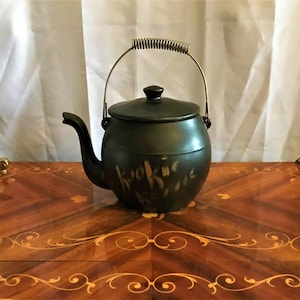 May include: A black ceramic cookie jar shaped like a teapot with a spring-loaded handle. The jar has the word "Kookies" written on the side.