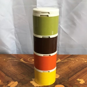 May include: A stackable container set with four sections in olive green, brown, orange, and yellow, each with a white lid. The containers are cylindrical and appear to be made of plastic. The set is standing upright.