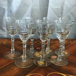 May include: Set of six clear glass stemmed drinking glasses with etched floral designs. The glasses have a fluted stem and a round base.