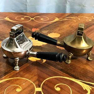 May include: Two vintage table lighters with black handles. One is silver and the other is gold.