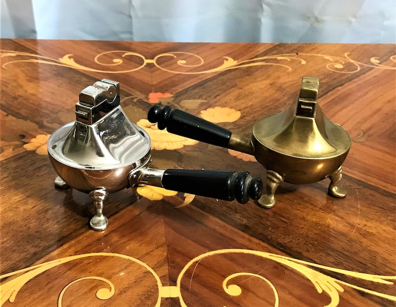 May include: Two vintage table lighters with black handles. One is silver and the other is gold.