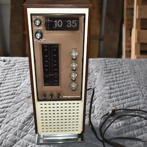 May include: Vintage Magnasonic AM/FM radio alarm clock. The clock displays 10:35. The radio has a brown wooden top and sides, a beige front with a speaker, and a silver base. It features a tuning dial, volume control, and radio frequency display.