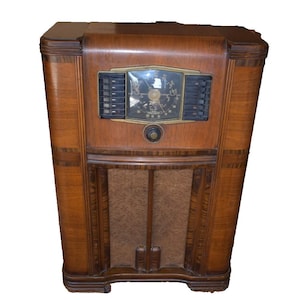 May include: An antique wooden radio cabinet with a dark brown finish. The radio features a dial, speaker cover, and various controls. The cabinet has a rectangular shape with rounded edges and decorative wood grain.