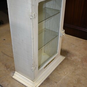 May include: White wooden cabinet with glass doors and shelves. The cabinet has a decorative floral design around the glass.