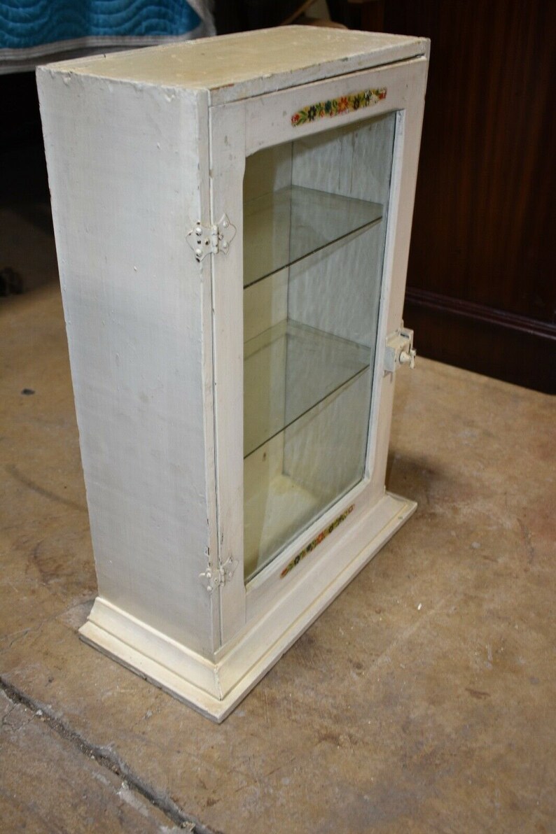 May include: White wooden cabinet with glass doors and shelves. The cabinet has a decorative floral design around the glass.