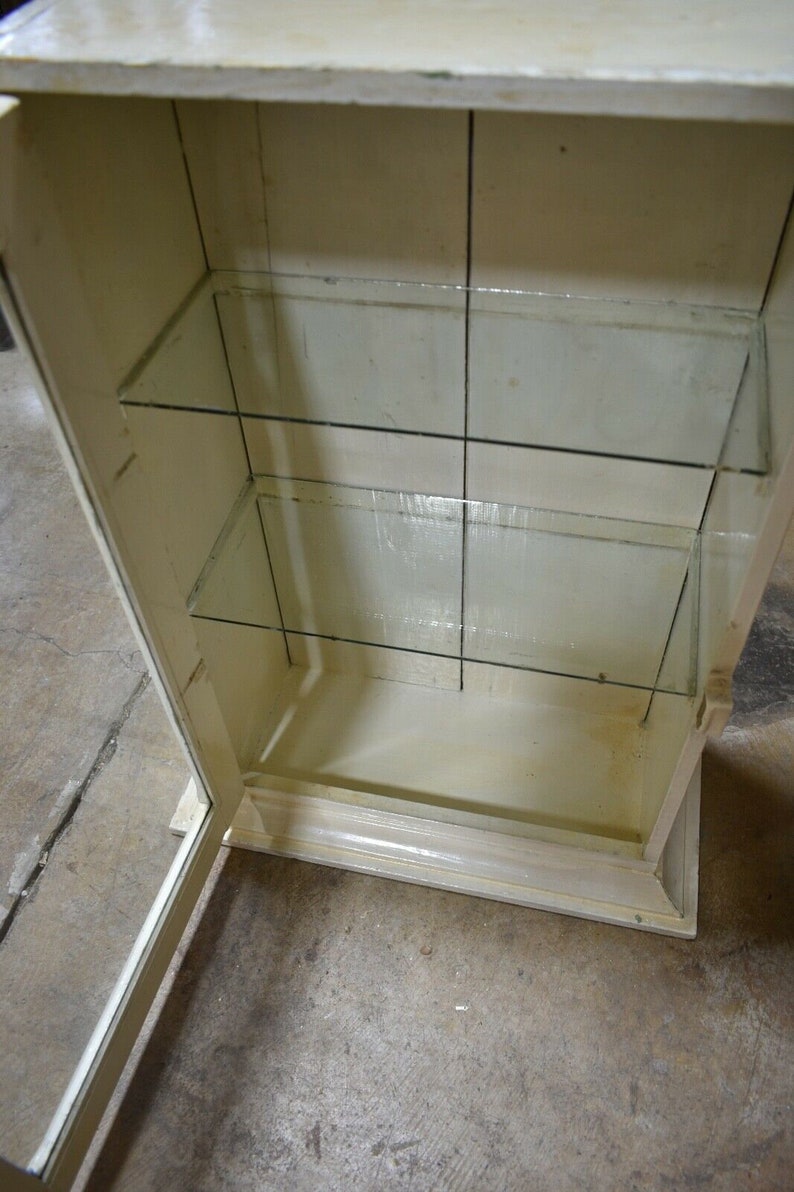 May include: A white wooden cabinet with glass shelves. The cabinet has a door that is open, revealing the empty shelves inside.