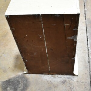May include: A white wooden cabinet with a brown wooden back. The cabinet has a simple design and is in good condition.