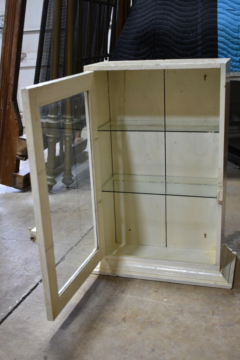 May include: A white wooden cabinet with a glass door and shelves. The door is open and the shelves are empty.