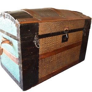 May include: An antique trunk with a domed top. The trunk features a combination of colors and textures, including black, brown, and a textured pattern. The sides are a light blue color. It has metal hardware and leather handles.