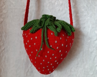 Puede incluir: Bolso bandolera de fresa roja tejido a ganchillo, con una parte superior verde con hojas y una correa roja. El bolso presenta detalles de semillas blancas y un cierre de cordón. Diseñado para llevar al hombro.