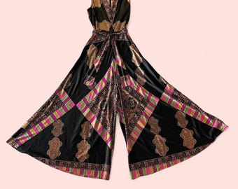 May include: A sleeveless jumpsuit featuring a deep V-neckline and a wide-leg silhouette. The garment is black with a vibrant pattern of gold-toned paisley shapes, pink and green striped geometric borders, and a matching tie-waist belt.