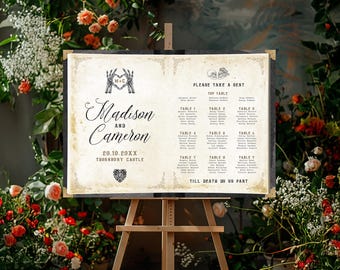 May include: A rectangular wedding seating chart on a wooden easel, featuring an aged parchment background with black text. It displays the names Madison and Cameron, the date 28.10.20XX, table assignments, and the phrase Till Death Do Us Part.