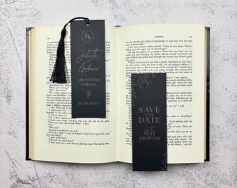 May include: Two rectangular black bookmarks with white text resting on an open book. One bookmark features the initials JA, the names Juliette and Andrew, the text ARE GETTING MARRIED, and the date 01.07.2022. The other reads SAVE THE DATE for the NEXT CHAPTER.