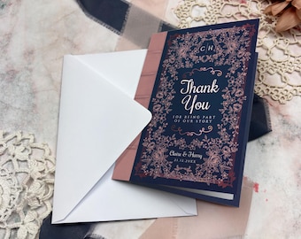 May include: A navy blue thank you card with floral design and the words "Thank You" in elegant script. The card is accompanied by a white envelope and a pink spine. The card reads "For being part of our story".