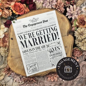 Op de afbeelding: Een nep-krantenadvertentie met de kop "We're Getting Married!" De krant heet "The Engagement Post" en heeft een foto van een ring met het woord "YES" erboven. De advertentie is omringd door bloemen.