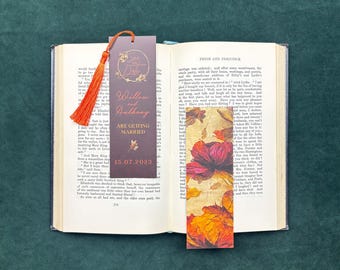 May include: Two rectangular bookmarks resting on an open book. One bookmark is dark brown with an orange tassel, featuring the text 'Save the Date', 'Willow and Anthony', 'ARE GETTING MARRIED', and '15.07.2023'. The other features a vibrant floral print.