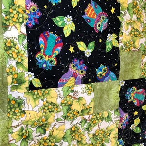 May include: A patchwork quilt featuring alternating fabric squares. Some squares display a black background with colorful, patterned owls, white dots, and green leaves. Other squares show green grapes on vines with yellow and green leaves.