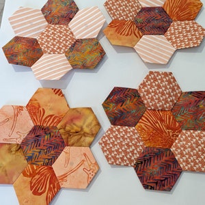 May include: Four hexagonal fabric patchwork designs in shades of orange, brown, and white. Each design features a different pattern, including stripes, floral prints, and geometric shapes.