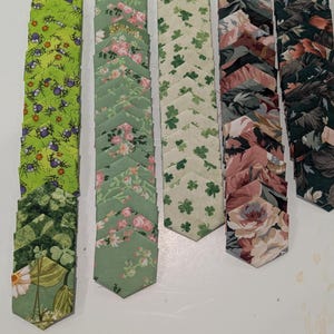 May include: A collection of fabric hexagons arranged in five vertical columns. The patterns include bright green with purple spiders, light green with pink flowers, cream with green shamrocks, and dark floral prints featuring roses and foliage.