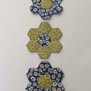 May include: Three fabric flower appliques in shades of blue and yellow. The flowers are made of hexagons and feature a daisy print.