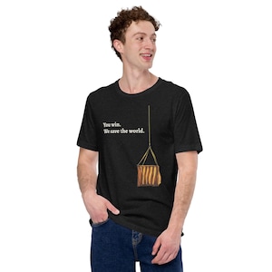 May include: Dark gray t-shirt with the text "You win. We save the world." and a graphic of a hanging object. The shirt is made of a soft material and has a classic crew neck.