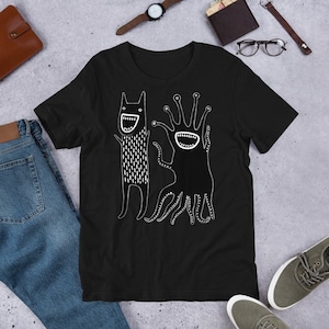 May include: Black t-shirt with a white graphic of two cartoon monsters. The monster on the left has a long, thin body with a large mouth and eyes. The monster on the right has a round body with a large mouth and many tentacles.