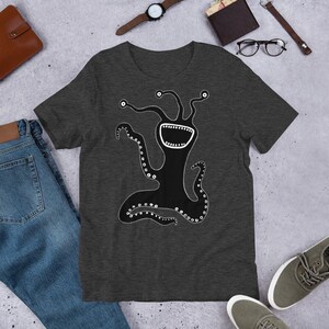 Könnte beinhalten: Ein dunkelgraues T-Shirt mit einem schwarz-weißen Motiv eines lächelnden, vieläugigen Wesens mit Tentakeln.
