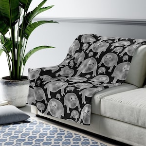 May include: A black fleece throw blanket with a white repeating pattern of frogs with grumpy expressions.