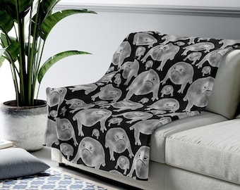 Può includere: Una coperta in pile nera con un motivo bianco ripetitivo di rane con espressioni accigliate.